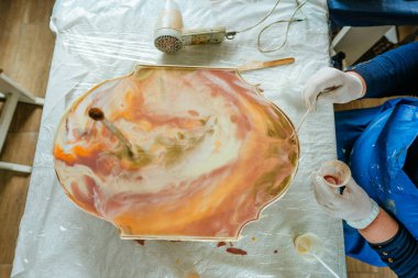 Ressam reçine sanatı tekniğinde saat yapıyor. Lastik eldiven takan kadın pigmentlerle sıvı reçine döküyor. Seçici odak.