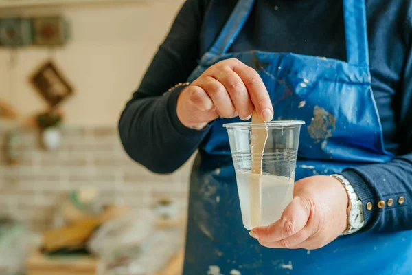 Resin sanat tekniğinde saat yapımında kullanılan malzemeleri hazırlayan sanatçı. Kadın epoksi reçinesinin iki bileşenini karıştırıp kimyasal reaksiyon yaratıyor. Seçici odak.