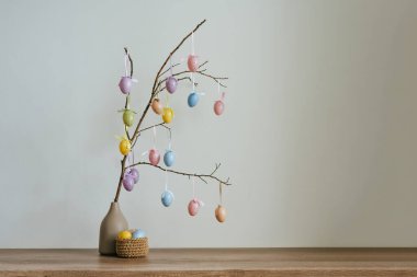 Paskalya yumurtalarıyla ağaç süsleme. Kapalı masa üzerindeki jüt sepetinin yanındaki vazoda..