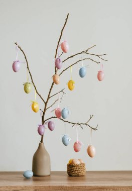 Paskalya yumurtalarıyla ağaç süsleme. Kapalı masa üzerindeki jüt sepetinin yanındaki vazoda..