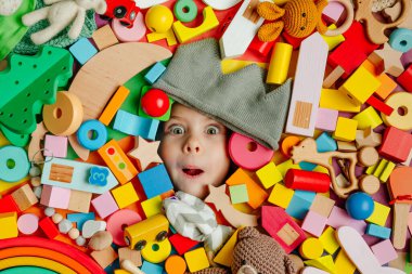 Etrafı oyuncaklarla çevrili bir kızın yüzü. Bir sürü ahşap renkli oyuncağın içinde yatıp eğlenen bir çocuk..