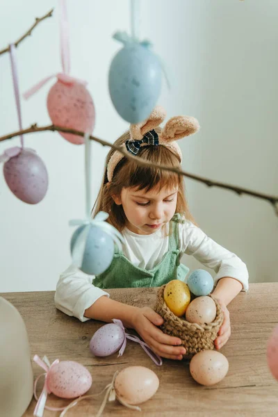 Tavşan kulaklı küçük kız içeride paskalya yumurtalarıyla bir ağacı süslüyor. Seçici odak.