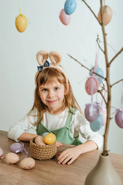 Tavşan kulaklı küçük kız içeride paskalya yumurtalarıyla bir ağacı süslüyor. Seçici odak.