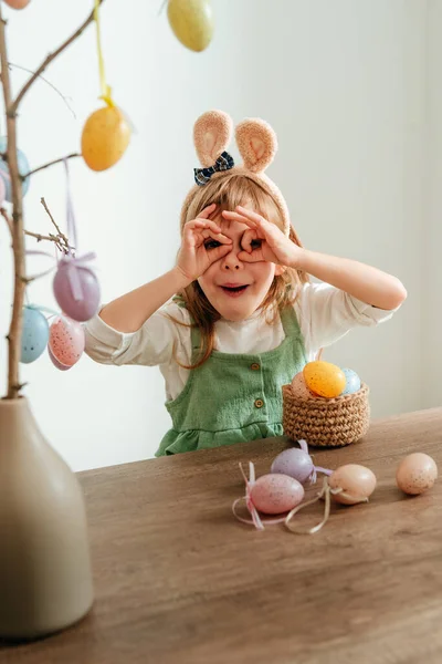 Tavşan kulaklı küçük kız içeride paskalya yumurtalarıyla bir ağacı süslüyor. Seçici odak.