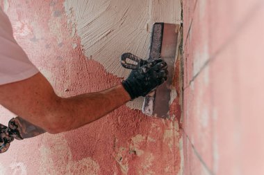 Erkek ellerinin balkon duvarına spatula ile macun harcı sürerken yakın plan..