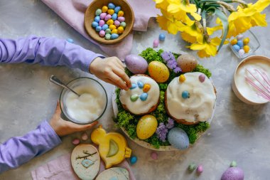 Paskalya pastalarını küçük renkli çikolata yumurtalarıyla süsleyen küçük bir kız. Şenlikli aşçılık konsepti. Düz yatıyordu.