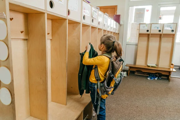 First day at school or kindergarten. Little girl with backpack hanging her jacket on a hanger in a wardrobe at school. Back to school concept.