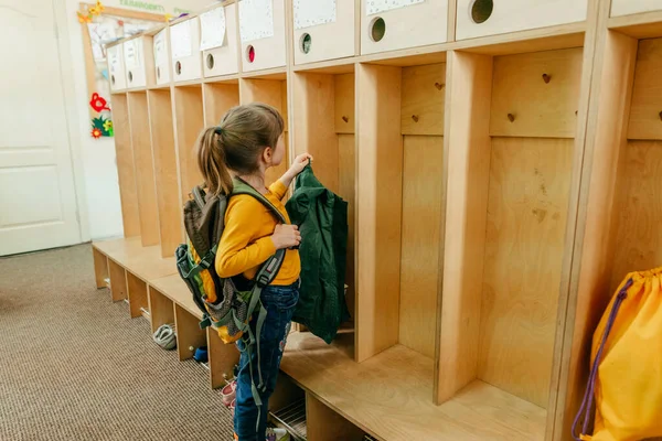 First day at school or kindergarten. Little girl with backpack hanging her jacket on a hanger in a wardrobe at school. Back to school concept.