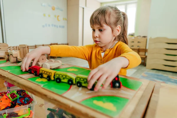 Anaokulunda ya da çocuk yuvasında tahta trenle oynayan küçük bir kız. Montessori eğitim kavramı.
