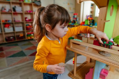 Anaokulunda ya da çocuk yuvasında oyuncak mobilyalarla ahşap evle oynayan küçük bir kız. Doğal malzeme oyuncakları ile erken gelişim. Montessori eğitim kavramı.