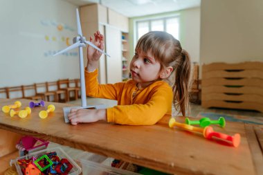Anaokulunda ya da çocuk yuvasında rüzgar enerjisiyle oynayan küçük bir kız..