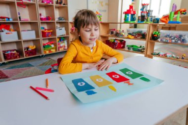 Anaokulunda ya da ilkokulda çöp konteynırlarıyla oynayan küçük bir kız. Eğitim konseptini geri dönüştürme.