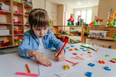 Little girl writing a word CAT playing with colorful plastic letters at kindergarten or primary school. Tactile and sensory methods for learning. Education concept.