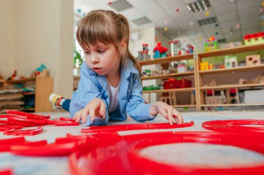 Anaokulunda ya da çocuk yuvasında yerde yatan kırmızı plastik oyuncaklarla oynayan küçük bir kız. Çocuk eğitimi konsepti.