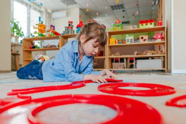 Anaokulunda ya da çocuk yuvasında yerde yatan kırmızı plastik oyuncaklarla oynayan küçük bir kız. Çocuk eğitimi konsepti.