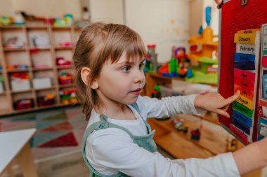 Küçük kız anaokulunda haftanın günlerini öğreniyor. Velcro tahtasındaki didactic materyaller okul öncesi eğitim için kullanılıyor. Seçici odak.