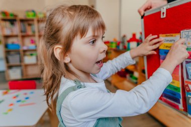 Küçük kız anaokulunda haftanın günlerini öğreniyor. Velcro tahtasındaki didactic materyaller okul öncesi eğitim için kullanılıyor. Seçici odak.