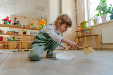Anaokulunda ya da çocuk yuvasında faraş ve süpürge kullanarak yerleri süpüren küçük bir kız. Montessori erken kalkınma eğitim kavramı.