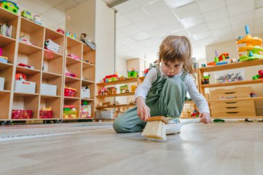 Anaokulunda ya da çocuk yuvasında faraş ve süpürge kullanarak yerleri süpüren küçük bir kız. Montessori erken kalkınma eğitim kavramı.