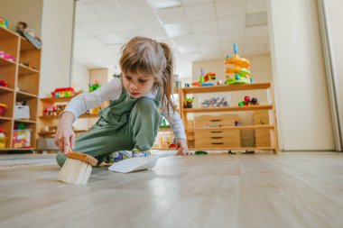 Anaokulunda ya da çocuk yuvasında faraş ve süpürge kullanarak yerleri süpüren küçük bir kız. Montessori erken kalkınma eğitim kavramı.