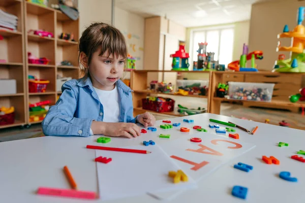Anaokulunda ya da ilkokulda renkli plastik harflerle oynayan küçük bir kız. Dokunsal ve duyusal öğrenme yöntemleri. Eğitim kavramı.