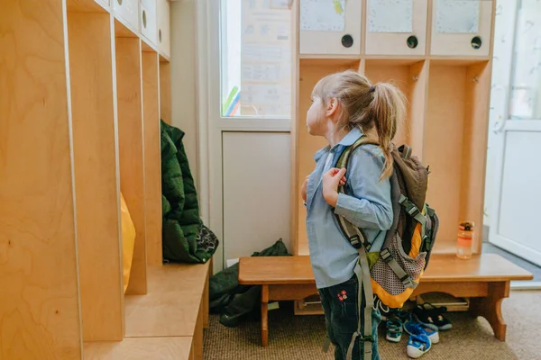 First day at school or kindergarten. Little girl with backpack looking at the kids wardrobe locker. Back to school concept.