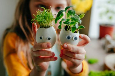 Evde yumurta kabuğu salatalıklı küçük bir kız ve oyuncak etiketli havuç tutuyor. Bayramlık Paskalya dekorasyonu için yaratıcı eğlenceli DIY fikri. Seçici odak.