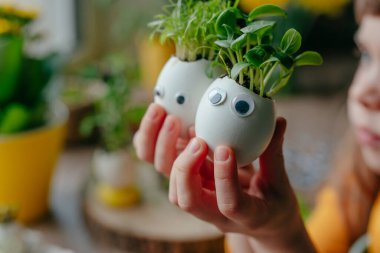 Evde yumurta kabuğu salatalıklı küçük bir kız ve oyuncak etiketli havuç tutuyor. Bayramlık Paskalya dekorasyonu için yaratıcı eğlenceli DIY fikri. Seçici odak.