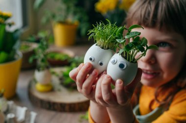 Evde yumurta kabuğu salatalıklı küçük bir kız ve oyuncak etiketli havuç tutuyor. Bayramlık Paskalya dekorasyonu için yaratıcı eğlenceli DIY fikri. Seçici odak.