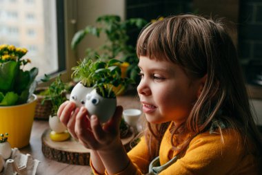 Evde yumurta kabuğu salatalıklı küçük bir kız ve oyuncak etiketli havuç tutuyor. Bayramlık Paskalya dekorasyonu için yaratıcı eğlenceli DIY fikri. Seçici odak.