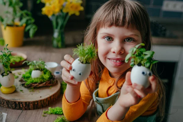 Evde yumurta kabuğu salatalıklı küçük bir kız ve oyuncak etiketli havuç tutuyor. Bayramlık Paskalya dekorasyonu için yaratıcı eğlenceli DIY fikri. Seçici odak.