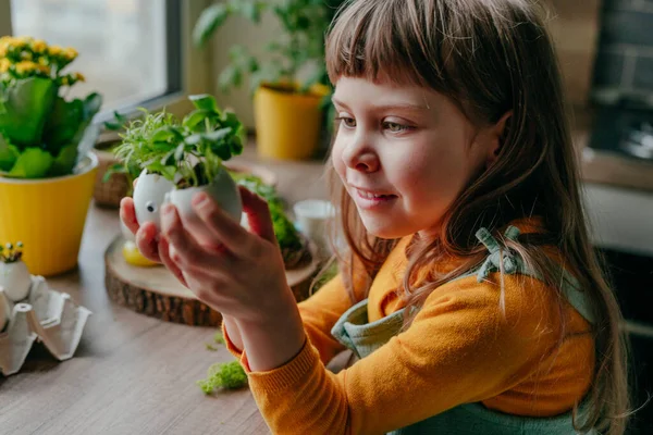 Evde yumurta kabuğu salatalıklı küçük bir kız ve oyuncak etiketli havuç tutuyor. Bayramlık Paskalya dekorasyonu için yaratıcı eğlenceli DIY fikri. Seçici odak.