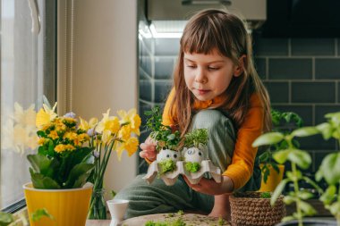 Evde oyuncak çıkartmalı yumurta kabuğu ve lahanalı küçük bir kız vardı. Bayramlık Paskalya dekorasyonu için yaratıcı eğlenceli DIY fikri. Seçici odak.
