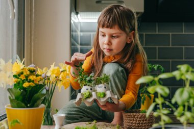 Evde oyuncak çıkartmalı yumurta kabuğu ve lahanalı küçük bir kız vardı. Bayramlık Paskalya dekorasyonu için yaratıcı eğlenceli DIY fikri. Seçici odak.
