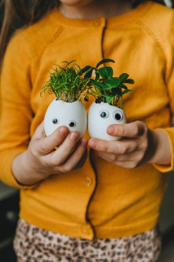 Salatalıklı yumurta kabuğu ve oyuncak etiketli havuç filizleri tutan küçük bir kız. Bayramlık Paskalya dekorasyonu için yaratıcı eğlenceli DIY fikri. Seçici odak.