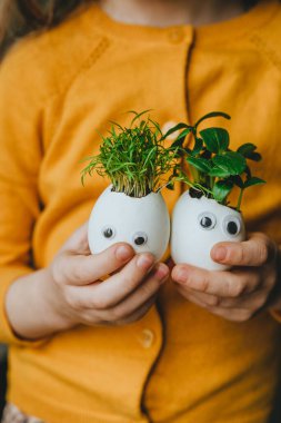 Salatalıklı yumurta kabuğu ve oyuncak etiketli havuç filizleri tutan küçük bir kız. Bayramlık Paskalya dekorasyonu için yaratıcı eğlenceli DIY fikri. Seçici odak.