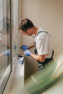 Genç adam tulum giyip balkonda su geçirmez silikon kazan kullanarak çatlakları kapatıyor. Lastik spatula kullanarak dolguyu çıkarıyorum. Seçici odak.