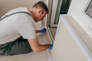 Genç adam, balkondaki su geçirmez silikon kalkanı kullanarak kapıyı mühürlemeden önce tulum giyip bant yapıştırıyordu. Seçici odak.