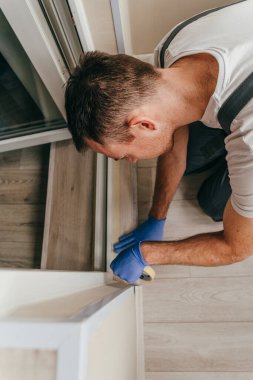 Genç adam, balkondaki su geçirmez silikon kalkanı kullanarak kapıyı mühürlemeden önce tulum giyip bant yapıştırıyordu. Seçici odak.