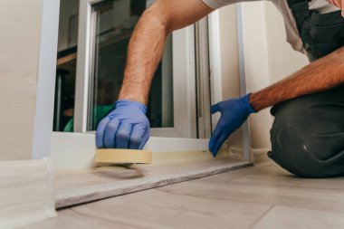 Genç adam, balkondaki su geçirmez silikon kalkanı kullanarak kapıyı mühürlemeden önce tulum giyip bant yapıştırıyordu. Seçici odak.