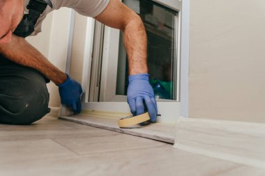 Genç adam, balkondaki su geçirmez silikon kalkanı kullanarak kapıyı mühürlemeden önce tulum giyip bant yapıştırıyordu. Seçici odak.