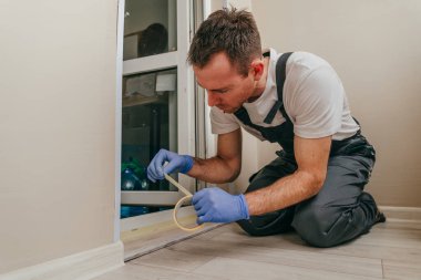 Genç adam, balkondaki su geçirmez silikon kalkanı kullanarak kapıyı mühürlemeden önce tulum giyip bant yapıştırıyordu. Seçici odak.