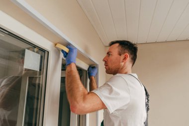 Balkona cam geçirmez silikon kalkanı yapıştırmadan önce tulum giymiş genç bir adam montaj bandı takıyordu. Seçici odak.