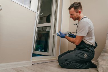 Tulum giyen genç adam balkonda su geçirmez silikon kalıntı kullanarak kapı ile süsleme arasındaki çatlakları kapatıyor..