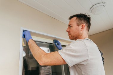 Balkona cam geçirmez silikon kalkanı yapıştırmadan önce tulum giymiş genç bir adam montaj bandı takıyordu. Seçici odak.