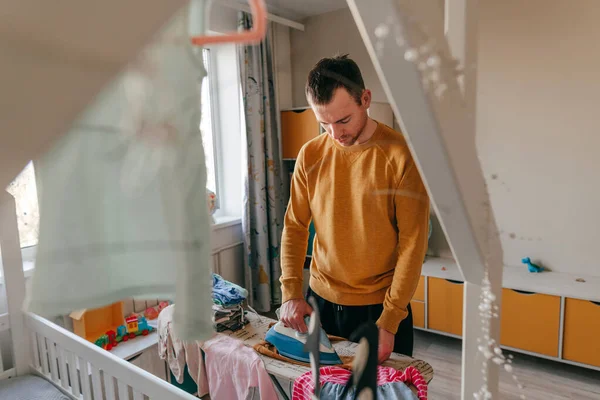 Young Man Ironing Baby Clothes Children Room Father Doing Chores — Stockfoto