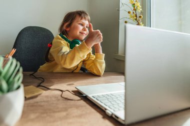 Beautiful little 5 years old girl using laptop sitting at the table in the room. Online education concept. Communication online, video chat. Family using technology at home. Selective focus.