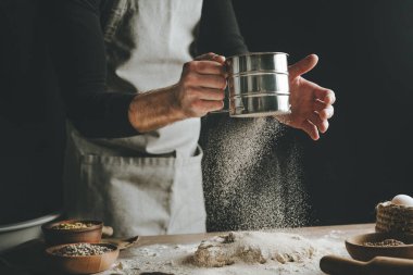 Hamur yoğurmak için un toplayan tanınmamış genç bir adam. Erkeklerin elleri arka planda ekmek yapıyor. Ellere odaklan..