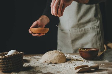 Tanınmayan genç bir adam koyu arkaplanda ayçiçeği ve kabak çekirdeği serpiştiriyor. Seçici odak.