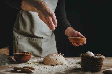 Tanınmayan genç bir adam koyu arkaplanda ayçiçeği ve kabak çekirdeği serpiştiriyor. Seçici odak.